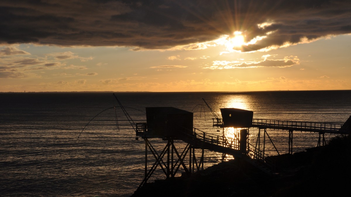 Cabanes de pêche devant un soleil couchant caché derrière un nuage