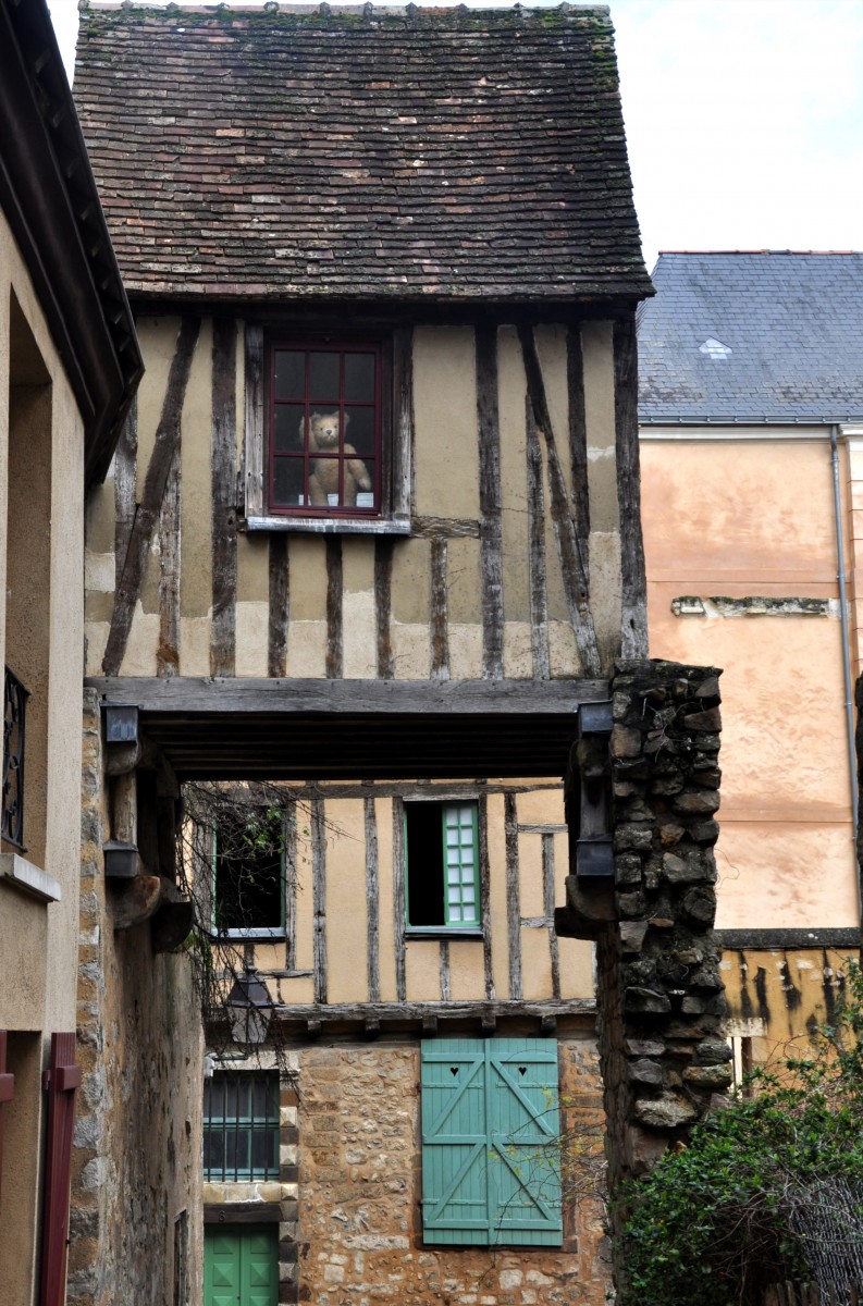 Petite peluche ourson qui fait coucou à une fenêtre de maison en colombages